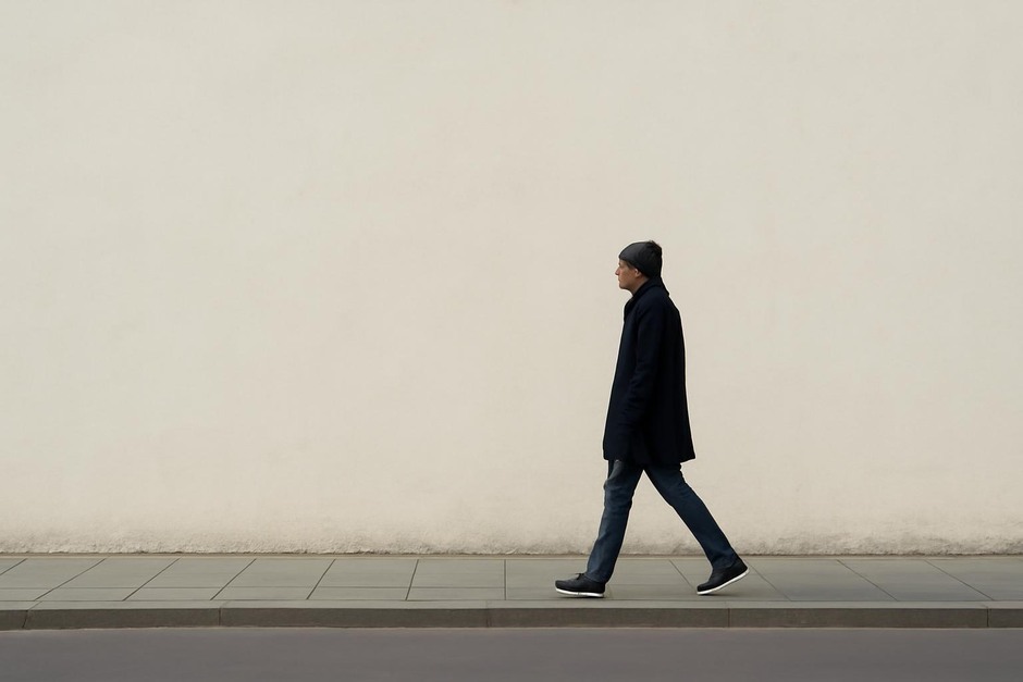 A minimal urban scene with a single figure against a pale wall, emphasizing negative space